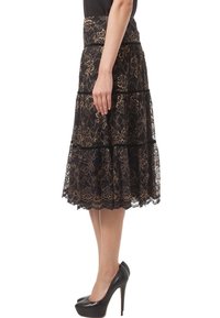 Black lace skirt with gold floral patterns, layered design, and black trim. Worn with black high heels, showing a fitted waistband.