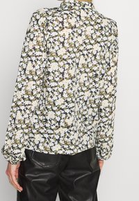 Bloemige blouse met lange mouwen, met een zwart, wit en groen patroon. Lichtgewicht, vloeiende stof, met een knoopsluiting aan de achterkant en een ronde zoom.