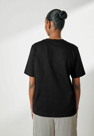 T-shirt en coton noir à manches courtes, col rond, coupe décontractée, associé à un pantalon large à rayures. Sans détails graphiques.