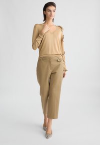 Top in maglia beige con scollo a V e maniche testurizzate, abbinato a pantaloni beige su misura con tasche frontali e un dettaglio con tie.