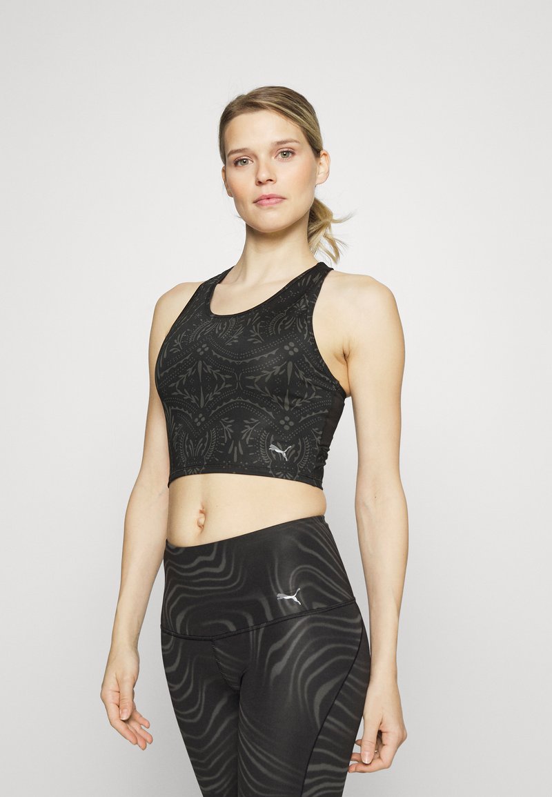 Top desportivo preto com um padrão texturizado, design de costas tipo nadador e logotipo na bainha. Usado com leggings pretas combinando, apresentando riscas onduladas.