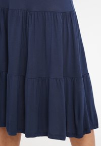 Marineblauwe gelaagde jurk van zacht katoen, met gatherings in de naden en een vloeiende silhouet tot aan de zoom.