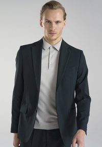 Ciemnozielona marynarka z dwiema przednimi kieszeniami, zestawiona z jasnoszarym polo z trzema guzikami. Gładki materiał, dopasowany fason.