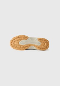 Sole of a sneaker featuring a tan rubber outsole with textured grip patterns and a white midsole. Smooth finish, ergonomic shape.