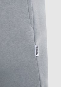 Pantalones deportivos grises hechos de tela suave, con un bolsillo lateral y una pequeña etiqueta blanca con el texto "SMILODON" cerca del dobladillo.