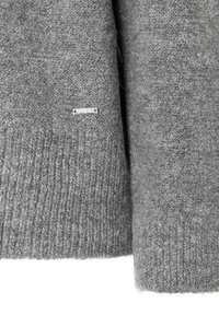 Grauer gestrickter Pullover mit geripptem Saum, ausgestattet mit einem kleinen metallischen Logostick auf der linken Seite. Weiche Textur und entspannter Schnitt.