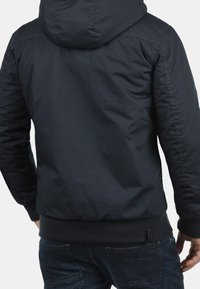 Veste à capuche bleu marine avec une texture lisse, un ourlet élastique et des détails de couture. Conçue pour la chaleur et le confort, avec une coupe décontractée.