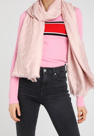Femme portant un pull rayé rose, un jean noir taille haute, et une écharpe rose clair drapée autour du cou et des épaules.