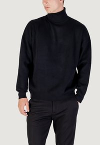 Zwarte coltrui van zachte stof met een losse pasvorm, verlaagde schouders en ribgebreide manchetten, in combinatie met zwarte broek. Eenvoudig en minimalistisch ontwerp.