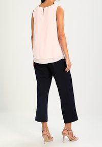 Top sin mangas de color rosa claro con detalle de ojal en la parte de atrás, combinado con pantalones cropped en navy y sandalias de tacón abierto rosas claras.
