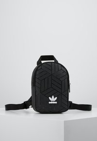 Svart ryggsäck med ett geometriskt texturerat mönster, försedd med blixtlåsstängning, justerbar rem och vit adidas-logotyp på framsidan.