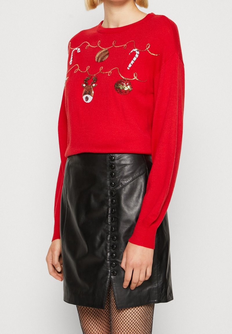 Rode trui met feestelijke borduursels, met ornamenten en zuurstokken. Gecombineerd met een zwarte leren rok, met knoopdetail en een split aan de voorkant.