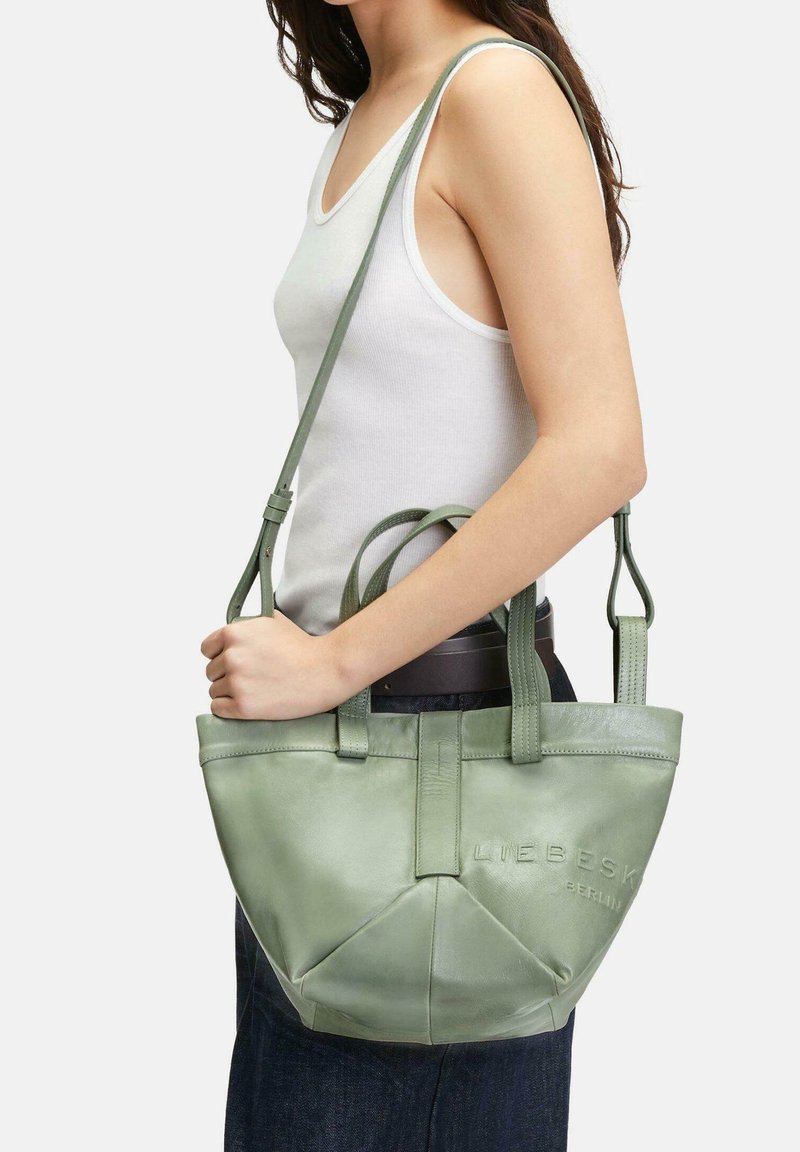 Zelená kožená taška přes rameno s dvojitými krátkými uchy a dlouhým nastavitelným popruhem, s hladkým povrchem a embosovaným logem.
