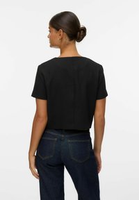 Svart cropped topp med korta ärmar, fyrkantig halsringning och slät textur. Kombinerad med högmidjade mörka denimjeans med bakfickor.