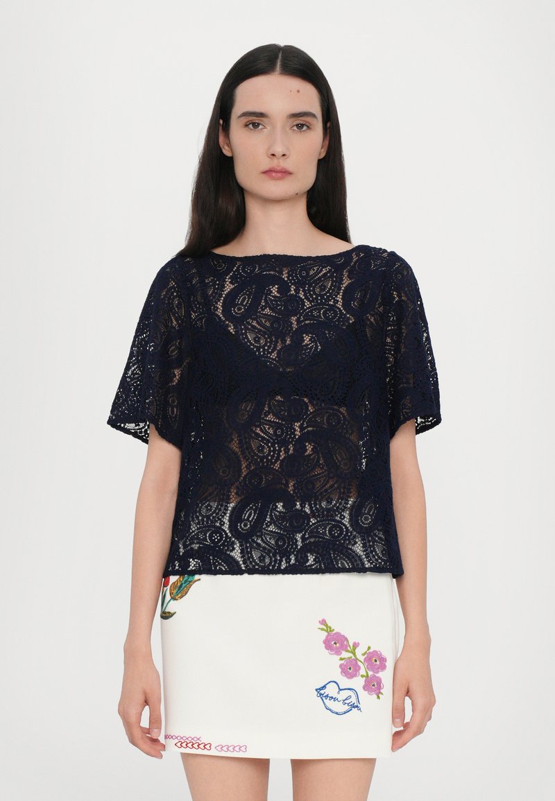 Navy lace top with short sleeves featuring an intricate paisley pattern, paired with a white skirt with floral embroidery and colorful accents.