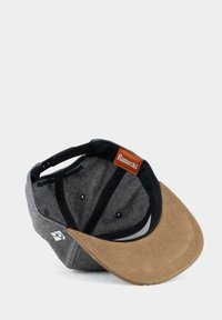 Gray cap with a tan suede visor, black accents, and a leather tag reading "Pumuckl." Interior features a smooth lining and ventilation holes.