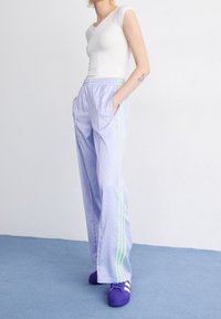 Ljust lila träningsbyxor med gröna ränder, tillverkade av ett mjukt tyg, med en avslappnad passform och sidofickor, i kombination med lila skor.