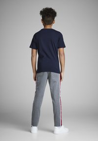 Mornarsko modra bombažna majica je kombinirana s sivimi trenirkami, ki imajo rdeče stranske črte in bele poudarke. Model nosi bele športne copate.