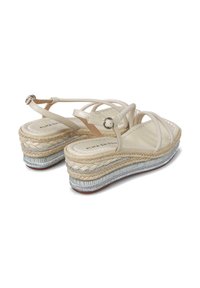 Sandalias de cuña con correas sintéticas en color crema, suela de yute estilo espadrille y un acento metálico plateado a lo largo de la base. Detalle de cierre con hebilla.