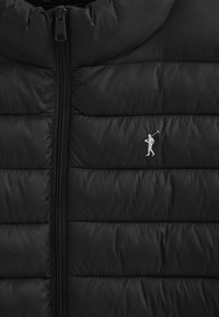 Sort puffer vest med quiltet tekstur og en frontlynlås. Indeholder et lille, sølvfarvet logo af en golfspiller. Glat, blankt stof.