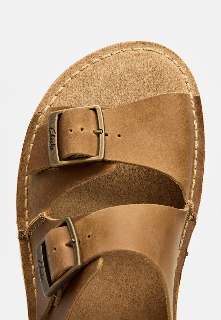 Sandale en cuir marron avec deux boucles réglables, bords cousus et texture lisse. Semelle intérieure moulée pour le confort et le soutien.