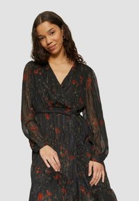 Schwarzes Blumen-Wickelkleid mit langen, durchsichtigen Ärmeln, V-Ausschnitt und tailliertem Bund. Es zeigt rote und grüne Blumenmuster sowie einen strukturierten Stoff.