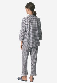 Navy og hvid ternet pyjamas sæt med lange ærmer og bukser, med flæsekanter og en løs pasform. Sutsko i samme mønster.
