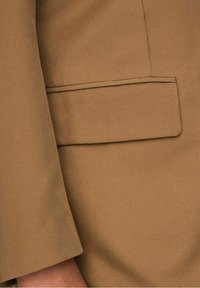 Close-up van een bruine blazer mouw en klepzak, met een gladde stoftextuur en verfijnde stiksel details.