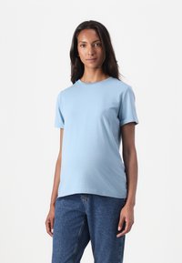 Tricou scurt, de culoare albastru deschis, dintr-un material moale, cu decolteu rotund, purtat cu blugi cu talie înaltă. Design simplu și curat.