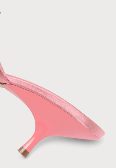 Chaussure rose en satin à petit talon courbé avec une pointe protectrice transparente sur fond clair.