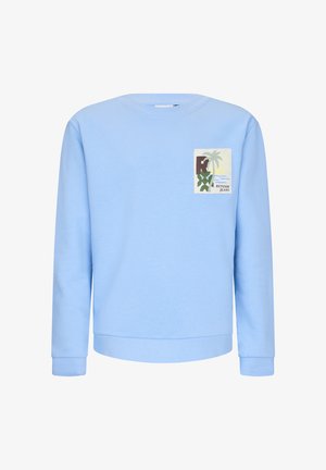 Jasnoniebieska bluza z okrągłym dekoltem i długimi rękawami, ozdobiona małą tropikalną naszywką z napisem "Retour Jeans" na lewej piersi.