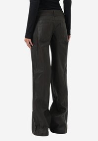 Mørkebrune læderbukser med vide ben, detaljeret syning, sidelommer og en glat tekstur. Set bagfra, fremhævet med subtile sømme.