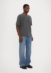 Grå oversized t-shirt med korte ærmer, der har et diskret logo. Sammen med lyseblå bredbenede jeans og sorte ankelstøvler.