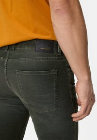 Mørkegrønne denimbukser med en tekstureret finish. Har en sort læderlap med "Camel Active"-logo på linningen og almindelige baglommer.