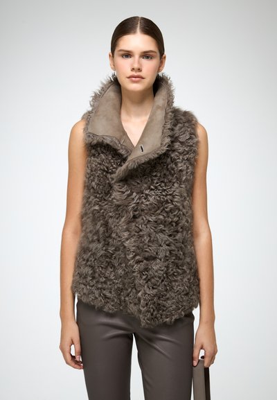 Gilet di pelliccia marrone con una texture morbida e soffice e un ampio colletto liscio. Scollo senza maniche, abbinato a pantaloni marroni attillati.