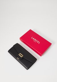 Svart lærplånbok med en foldet klaff og gullhardware som har et firkantet preg, ved siden av en rød Lancel Paris-boks.