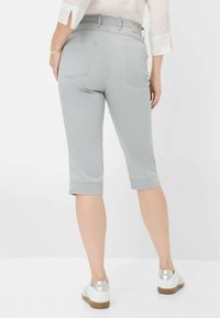Pantaloni capri grigi chiaro con una texture liscia, orli arrotolati e due tasche posteriori. Indossati con scarpe bianche e hardware minimal.