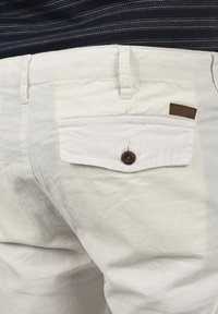Witte katoenen broek met een achterzak met knoopsluiting en een bruine leren label. Soepele textuur met een subtiele glans.