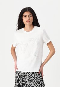 Vit t-shirt med kort ärm som har en design av tre konturerade rosetter gjorda av skimrande rhinestones. Mjuk, slät bomullsmaterial.