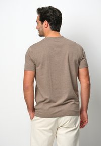 T-shirt marrone a maniche corte in tessuto morbido, con colletto girocollo classico e vestibilità comoda, abbinato a pantaloni color crema.