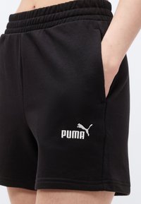 Μαύρα σορτς Puma με ελαστική μέση, το χέρι του φορέα στην πλαϊνή τσέπη και λευκό λογότυπο Puma στον αριστερό μηρό.