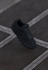 Sneaker Nike Air Force 1 preto com sobreposições de couro e texturizadas, com bico arredondado, atacadores planos e sola de borracha.