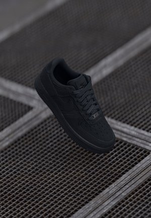 Crna Nike Air Force 1 tenisica s kožnim i teksturiranim preklopima, okruglim prstom, ravnim vezicama i gumenim đonom.