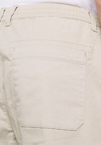 Pantalons en coton beige avec une taille élastique. Dotés d'une poche arrière avec des détails de couture. Texture douce et lisse.