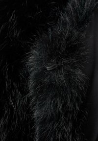 Tessuto in pelliccia sintetica nera con fibre lunghe e morbide e una texture leggermente lucida. Presenta un accento cordonato vicino al bordo. Sfondo scuro.