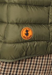 Oliwkowa kurtka puchowa z okrągłą pomarańczową naszywką "Save the Duck". Posiada pikowaną teksturę oraz gładki materiał z kontrastowym brązowym wzorem w kratę poniżej.