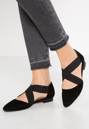 Czarne zamszowe baleriny z ostrym noskiem, z elastycznymi krzyżującymi się paskami i niskim obcasem. Noszone z wytartymi szarymi dżinsami.