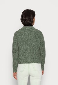 Groene, gestructureerde gebreide trui met een hoge hals en een cropped pasvorm, gecombineerd met lichtgroene, geribbelde broek. Geen zichtbare hardware of patronen.