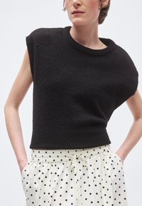 Μαύρο πουλόβερ με κοντά μανίκια, στρογγυλή λαιμόκοψη και υφή υφάσματος, συνδυασμένο με κρεμ παντελόνι με μαύρα πουά και ελαστική μέση.