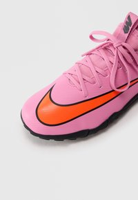 Rosa idrettssko med en oransje Nike-svush, svart såle og rosa snører bundet i en sløyfe mot en hvit bakgrunn.